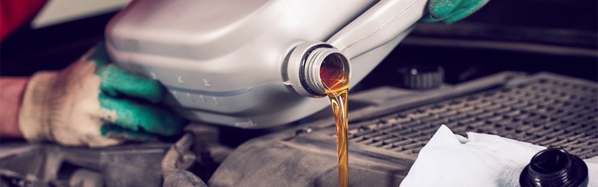 Auto mechanic replacing and pouring fresh oil into engine during maintenance at garage repair service station -